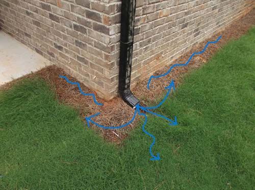 A drainpipe is sitting on the side of a brick building next to a lawn.