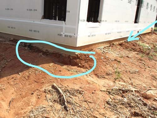 A blue arrow points to a hole in the ground next to a house under construction.