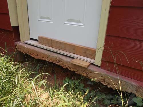 A white door is sitting on the side of a red house.