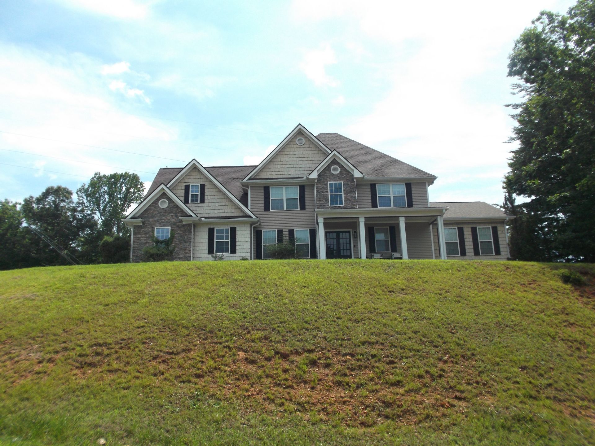 Large stone house with a gray roof on a grassy hill under a partly cloudy sky