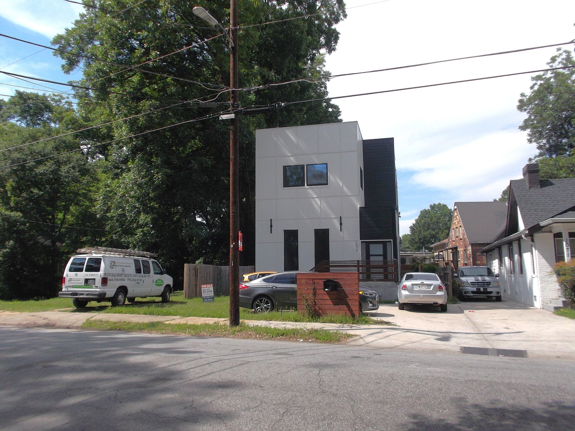 Modern white building on a street corner with parked cars and large trees nearby