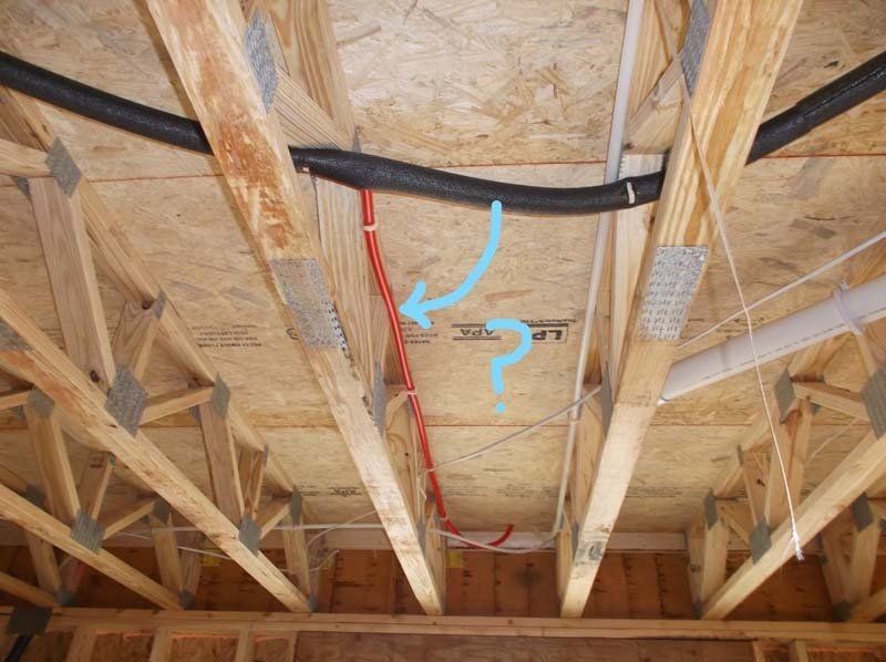 A blue arrow points to a red wire in the ceiling of a house under construction.
