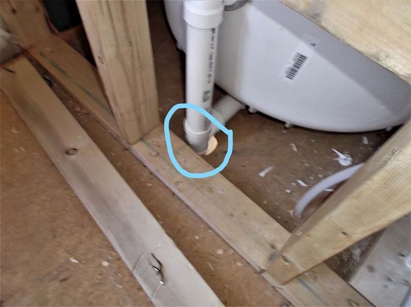 A white toilet is sitting in a wooden frame next to a pipe.