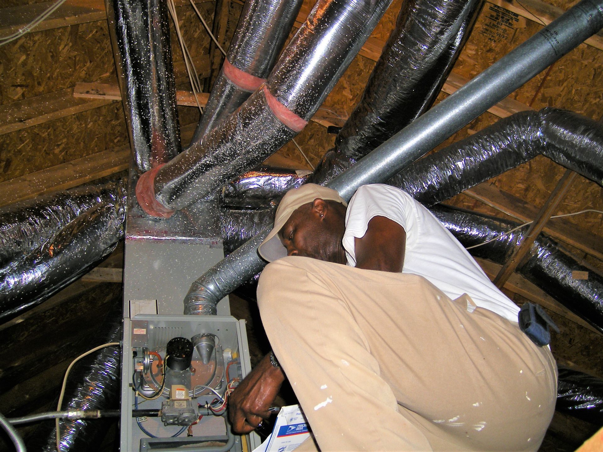 A man is working on an air conditioner in an attic
