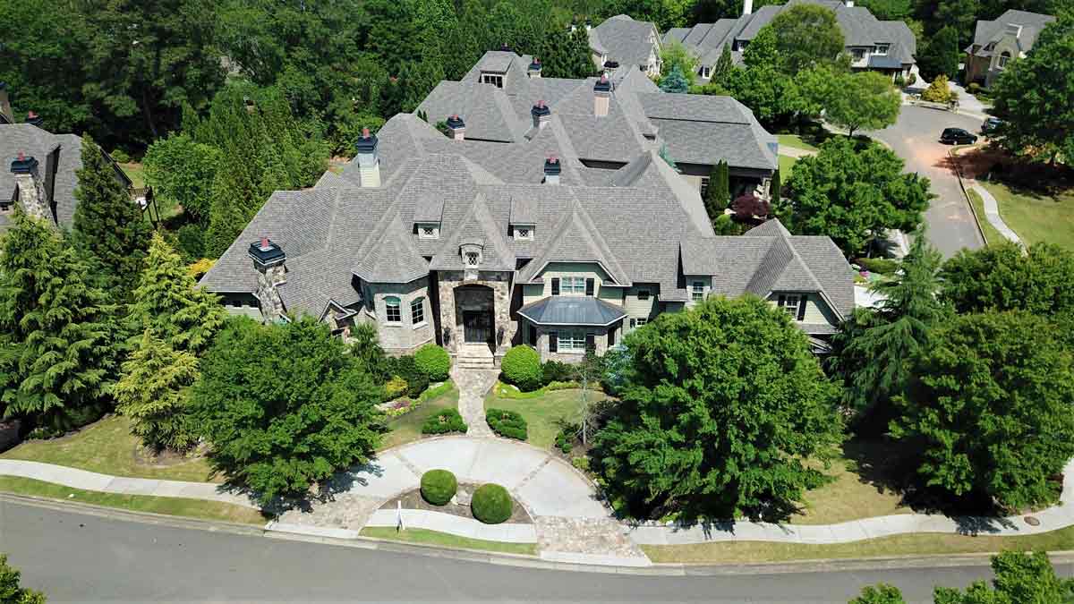 An aerial view of a large house in a residential neighborhood surrounded by trees.