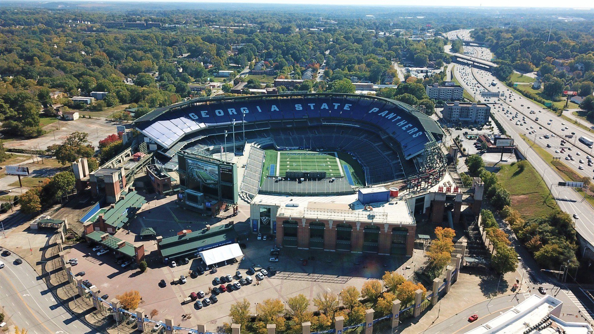 An aerial view of a football stadium surrounded by trees and a highway.
