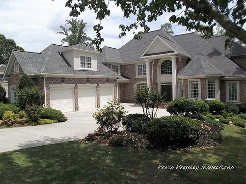 A large brick house with a gray roof and white garage doors
