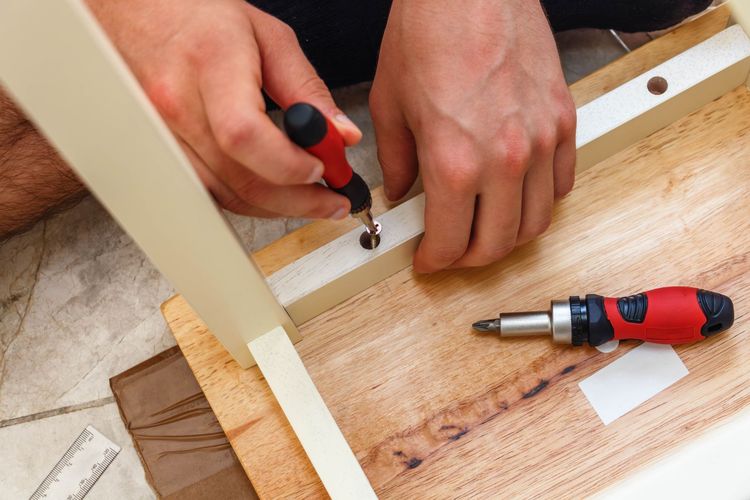 Una persona assembla un mobile con un cacciavite, fissando una vite a una gamba di legno.