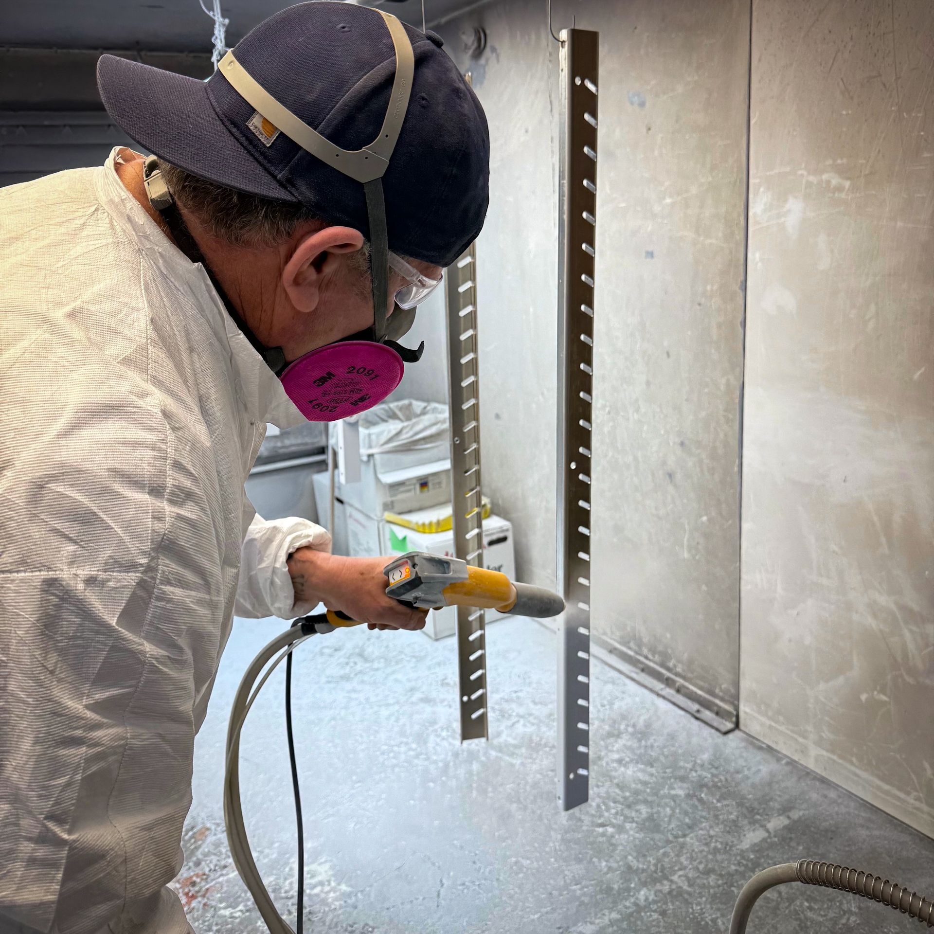 A man in a protective suit is spray painting a piece of metal.