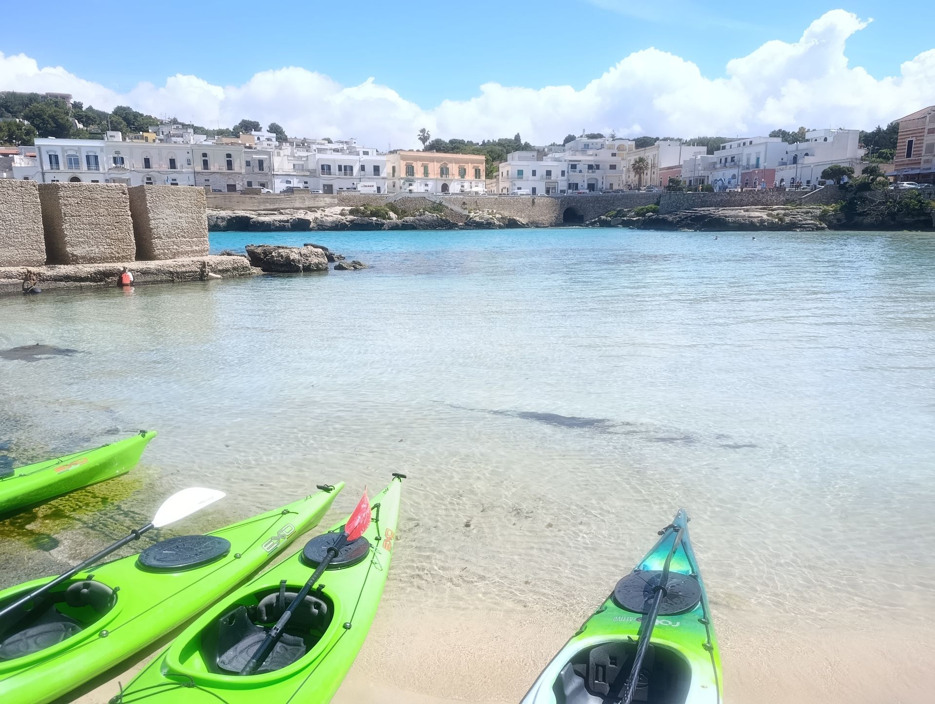 Kayak verde brillante su una spiaggia tranquilla con acqua cristallina e bianchi edifici sul lungomare sullo sfondo.