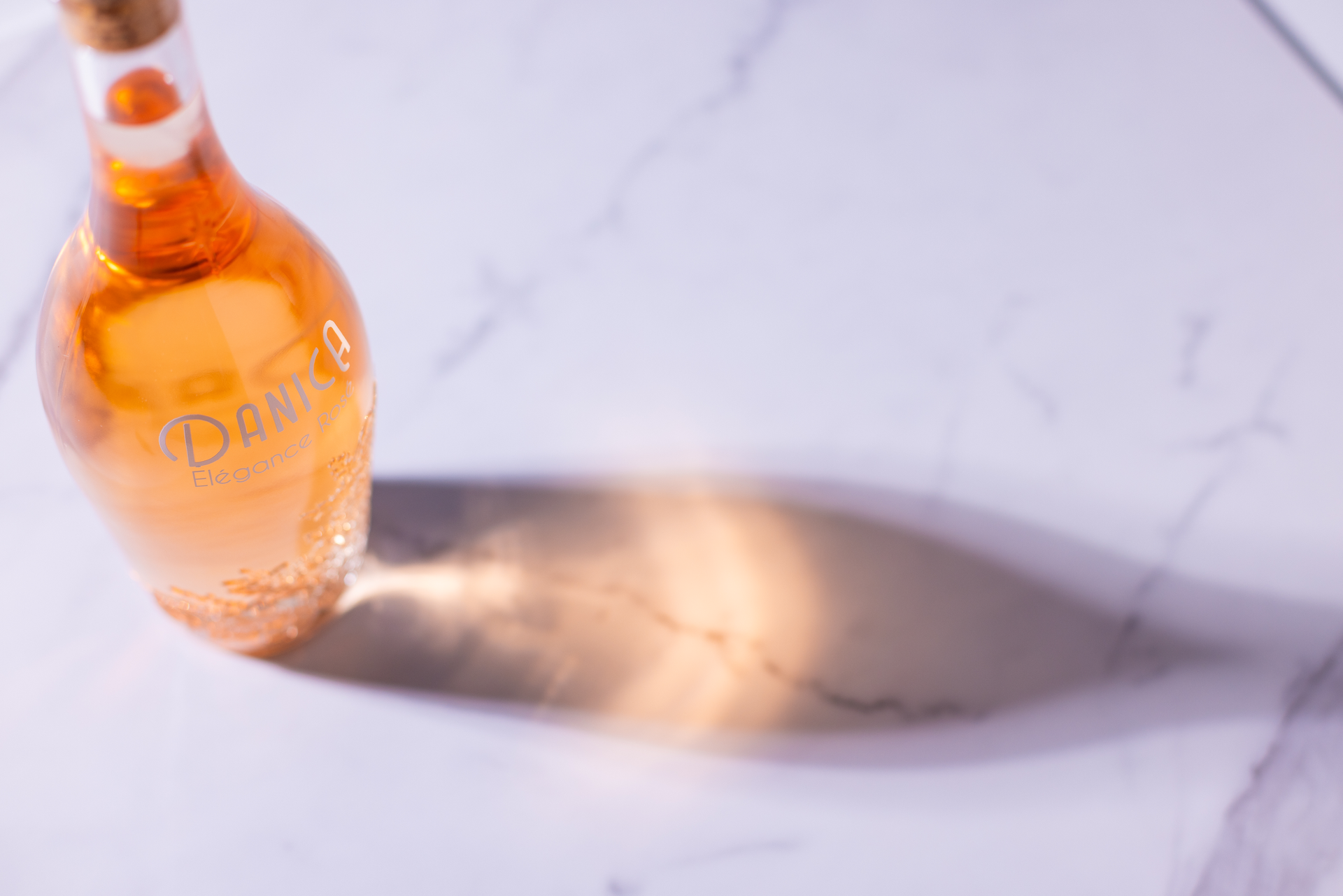 Bottle of orange-colored liquid with a cork, casting a long shadow on a white marble surface.
