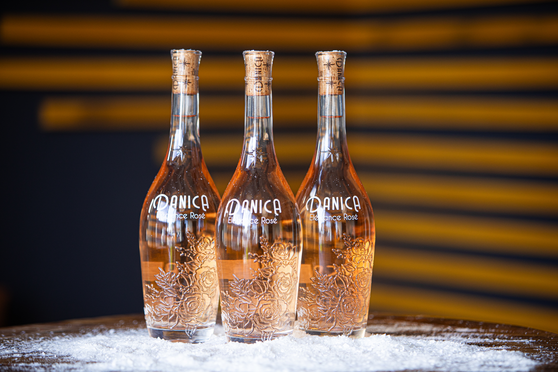 Three clear bottles with corks, filled with pink liquid, on a surface dusted with white.