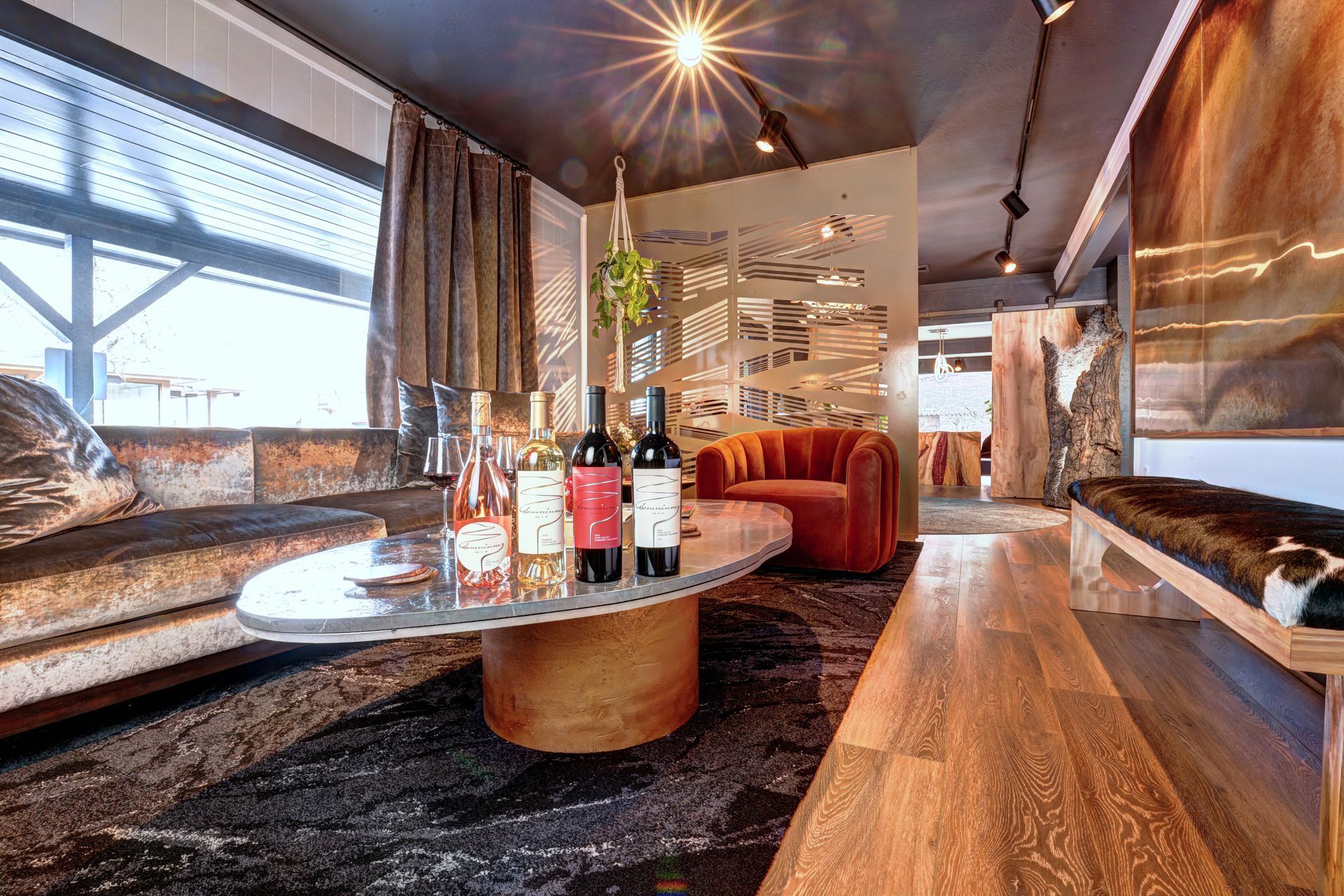 Cozy wine bar with couch, bench, and round coffee table displaying bottles of wine.
