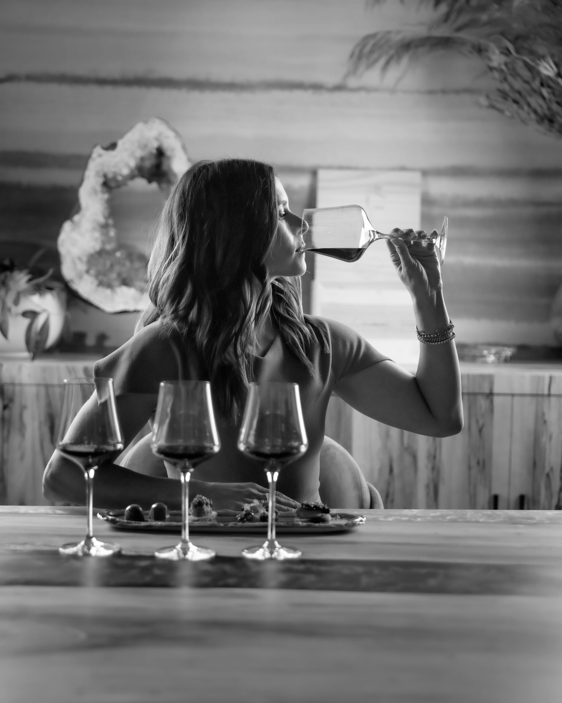 Woman drinks red wine at a table set with three glasses. Black and white photo.