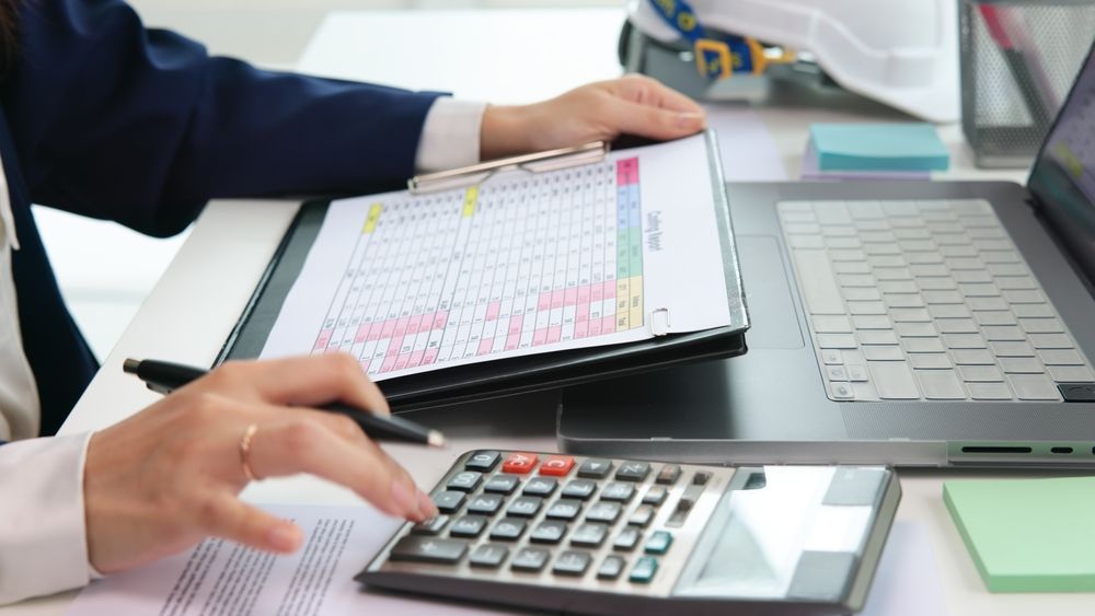 A person is sitting at a desk using a calculator and a laptop.