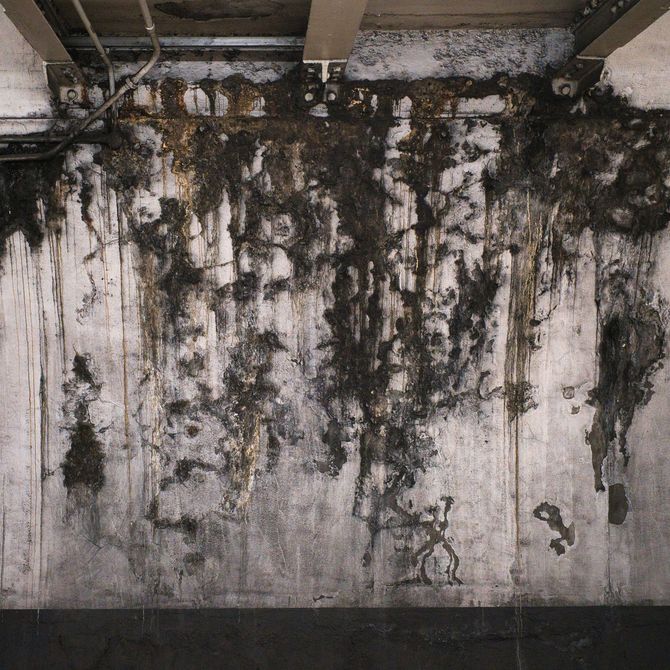 Mold and water stains streaking down a dirty concrete wall under exposed beams