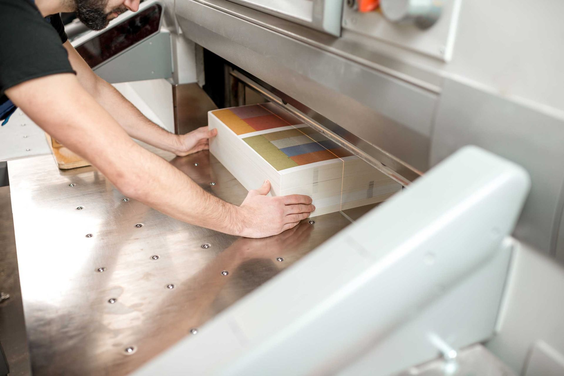 A man is lining up a stack of paper in the cutting machine at a printing shop.