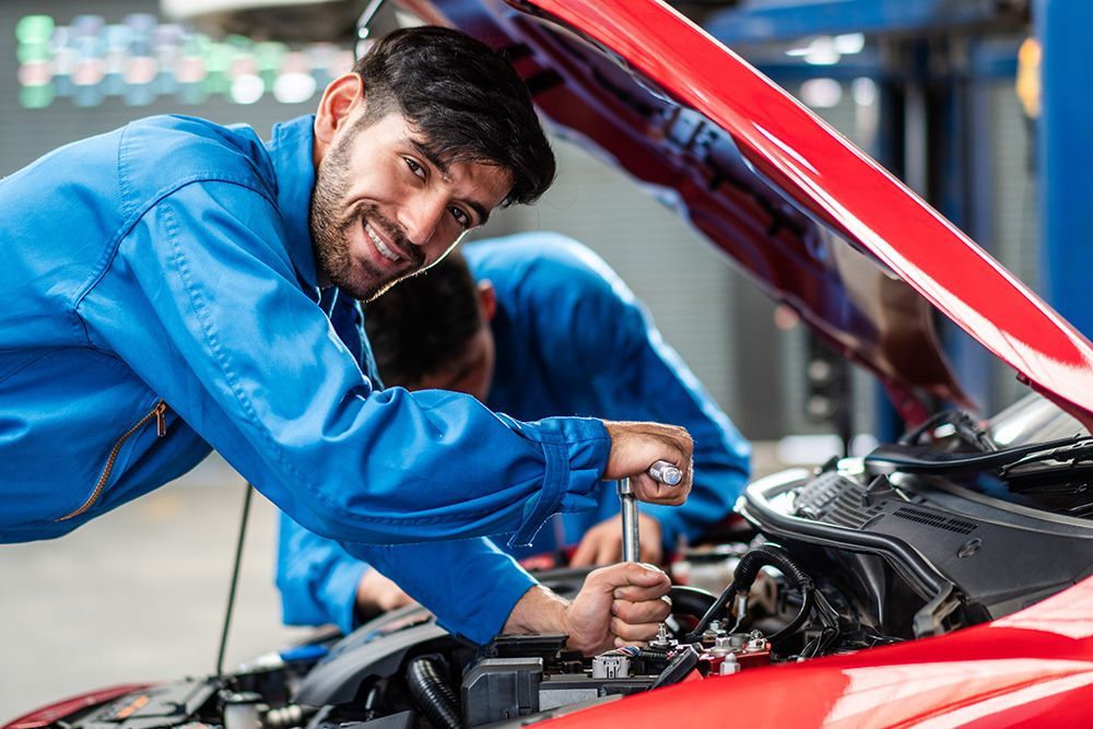 Two mechanics are working on a red car in a garage.