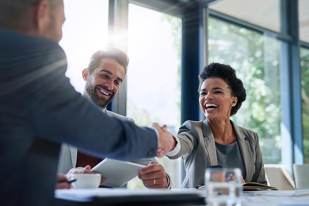A man and a woman are shaking hands while sitting at a table.