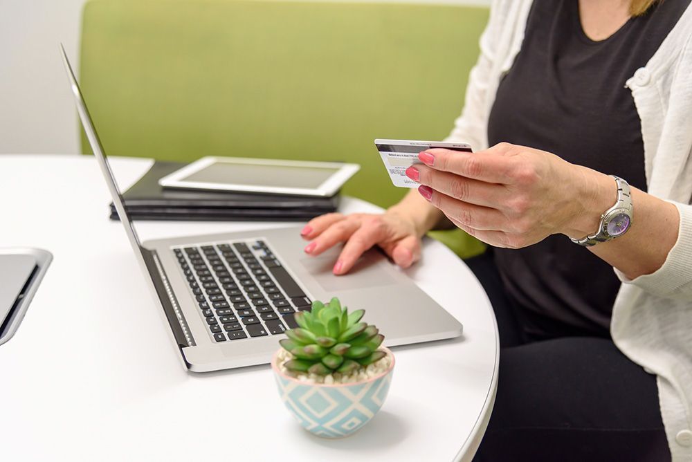 A woman is holding a credit card while using a laptop computer.