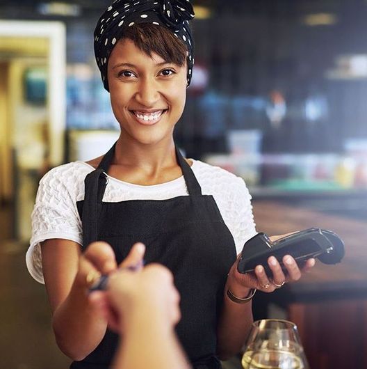 A woman in an apron is smiling while holding a credit card reader.