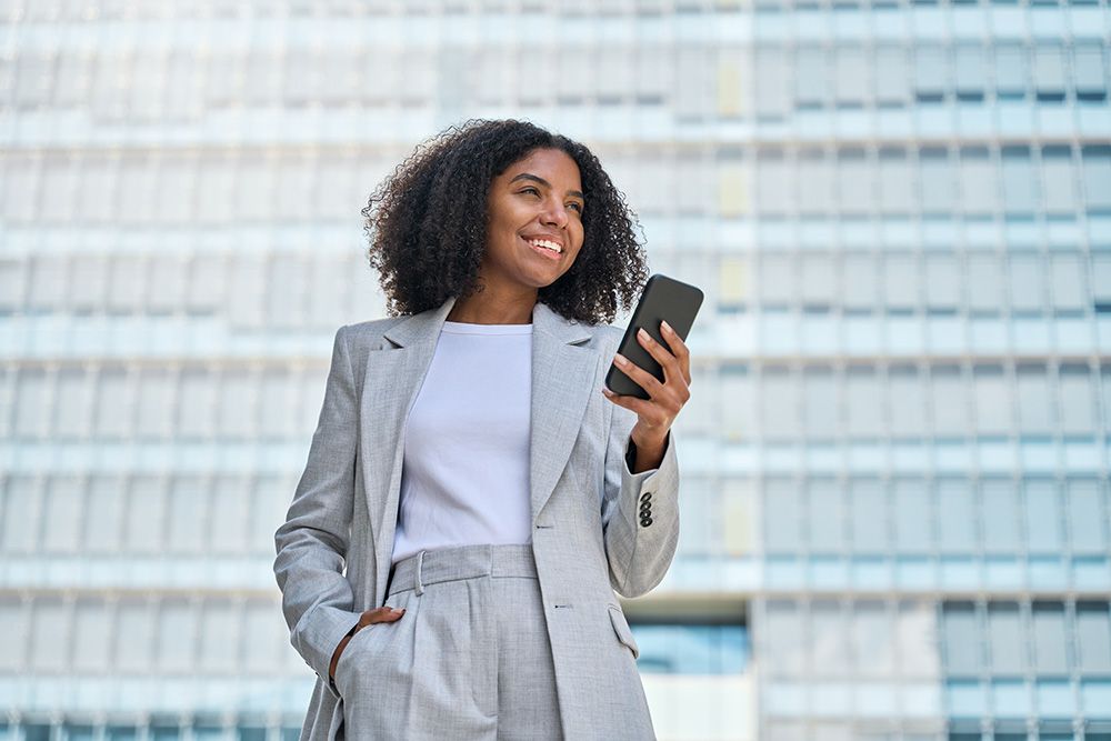 A woman in a suit is holding a cell phone in front of a building.