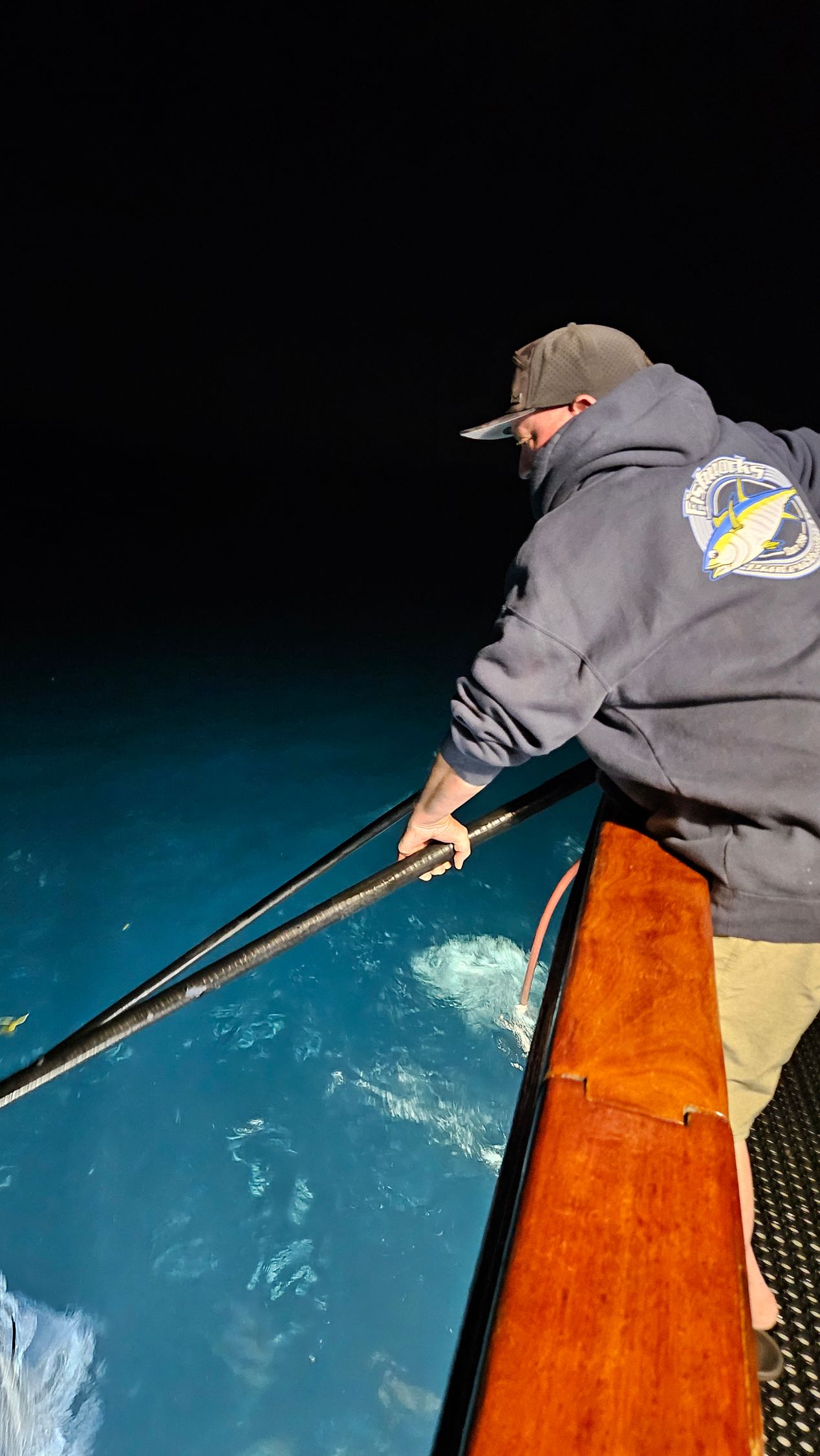 People fishing from a boat near a rocky shore; bright sunlight.