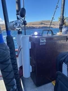 Fishing rods and tackle box on a boat with a view of the ocean and hills.