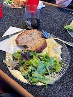 Plate of meatloaf, salad, and mashed potatoes, with a glass of red wine on a table.