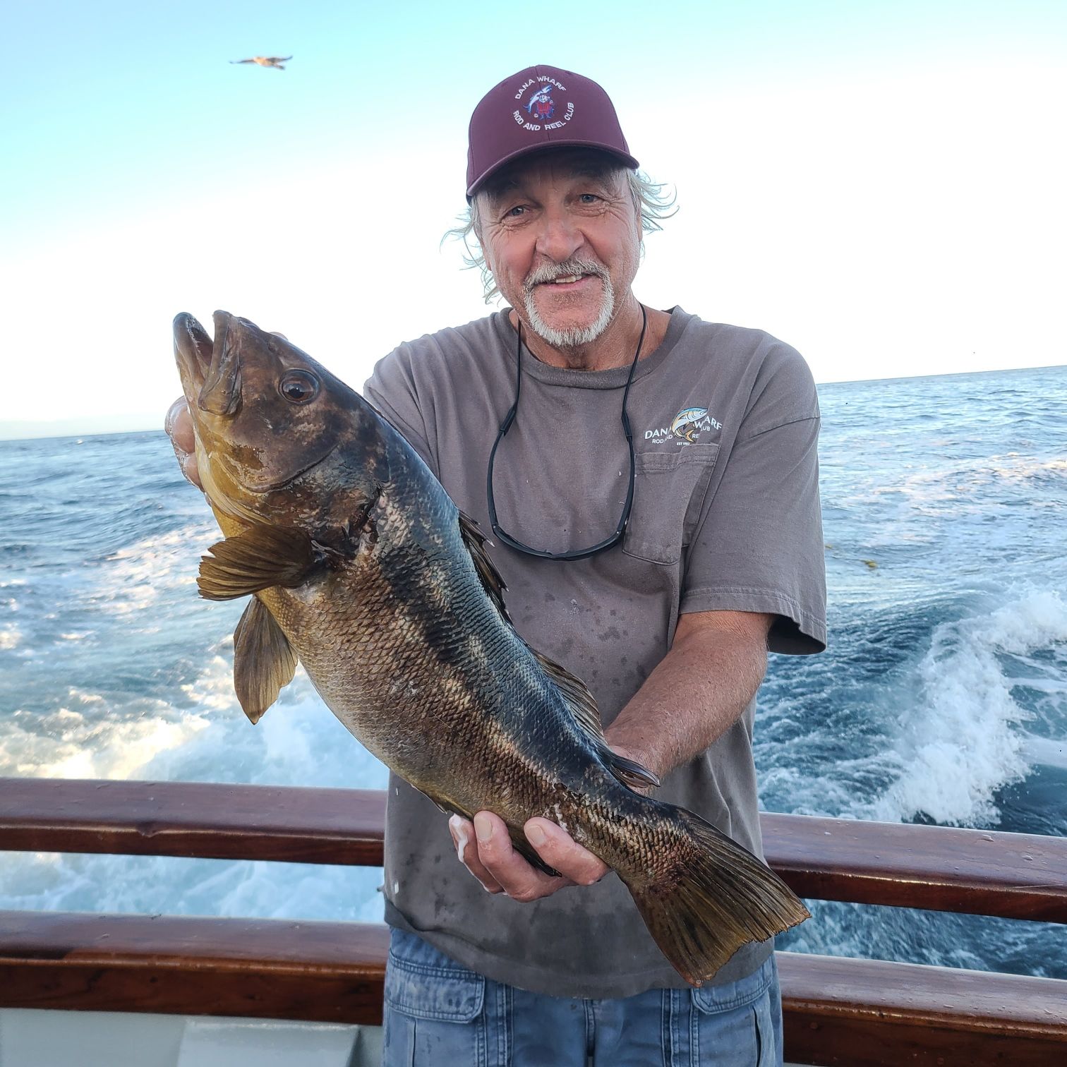 Two men on a boat holding a large speckled fish at night.