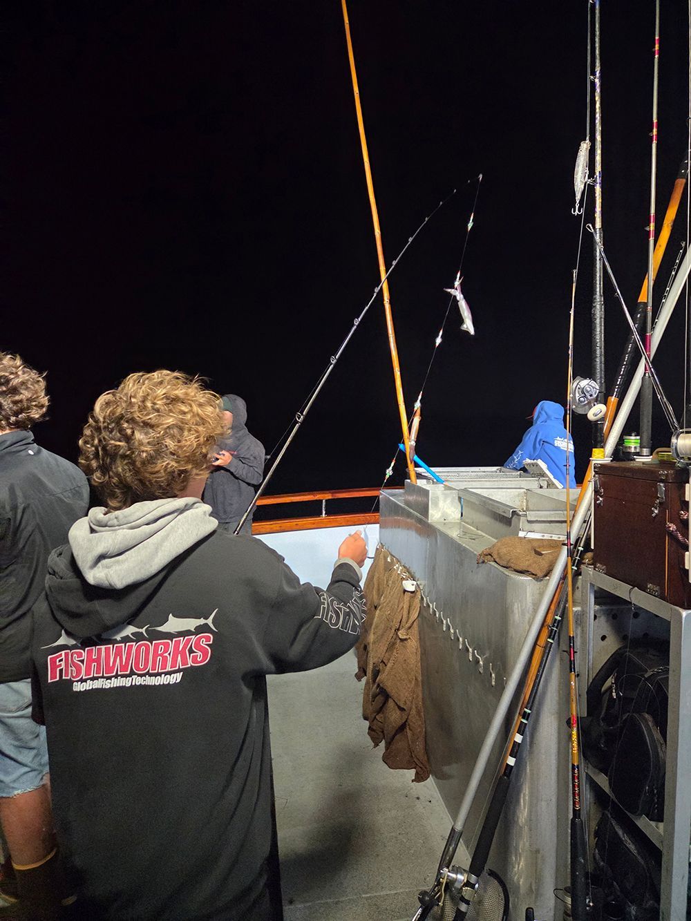 Person on boat fishing at night; several fishing rods visible.
