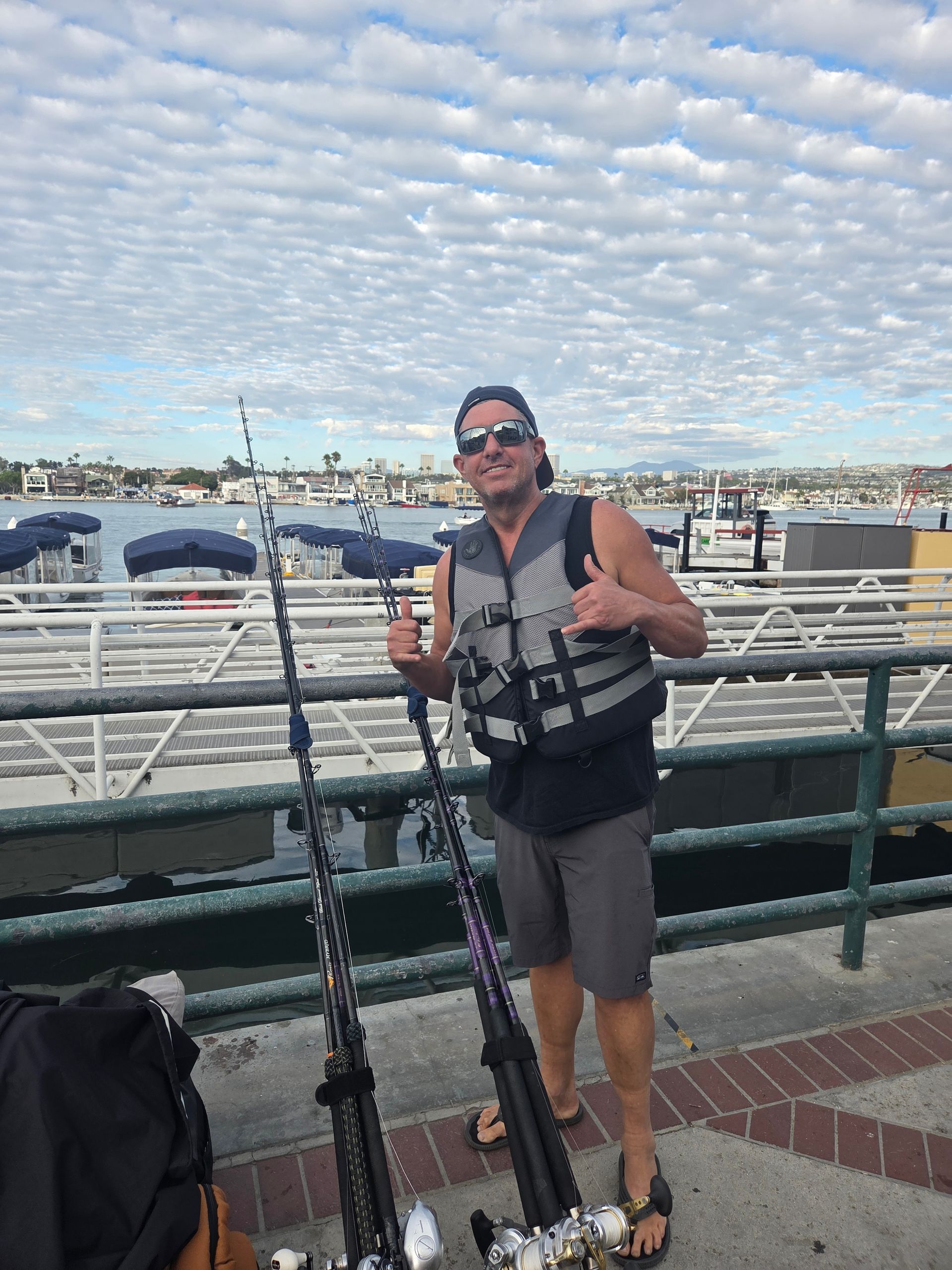Man on a boat holding a large, dark-colored fish. Mountains and ocean in the background.