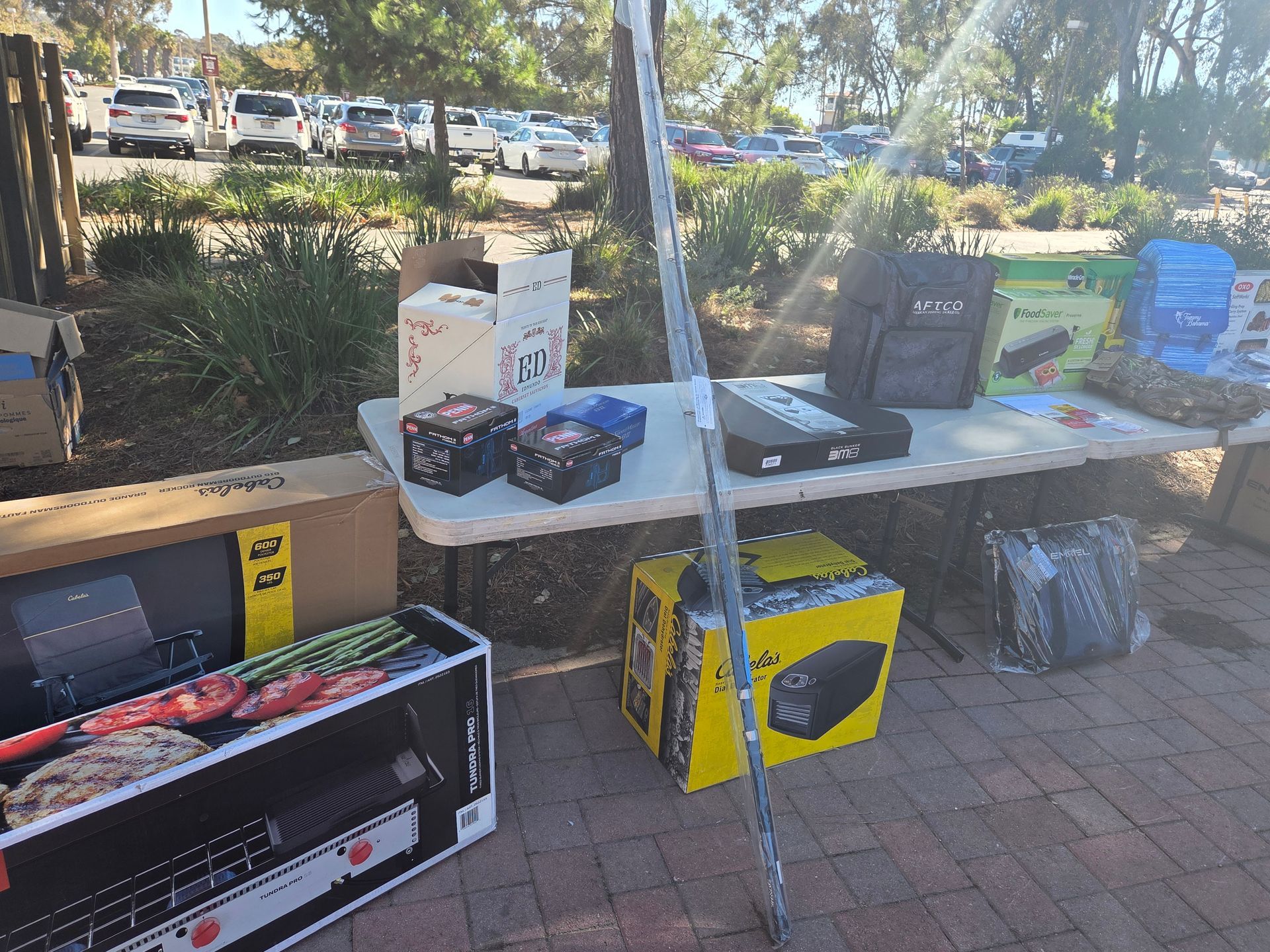 Table with various items for sale outdoors, including boxes, electronics, and gifts.
