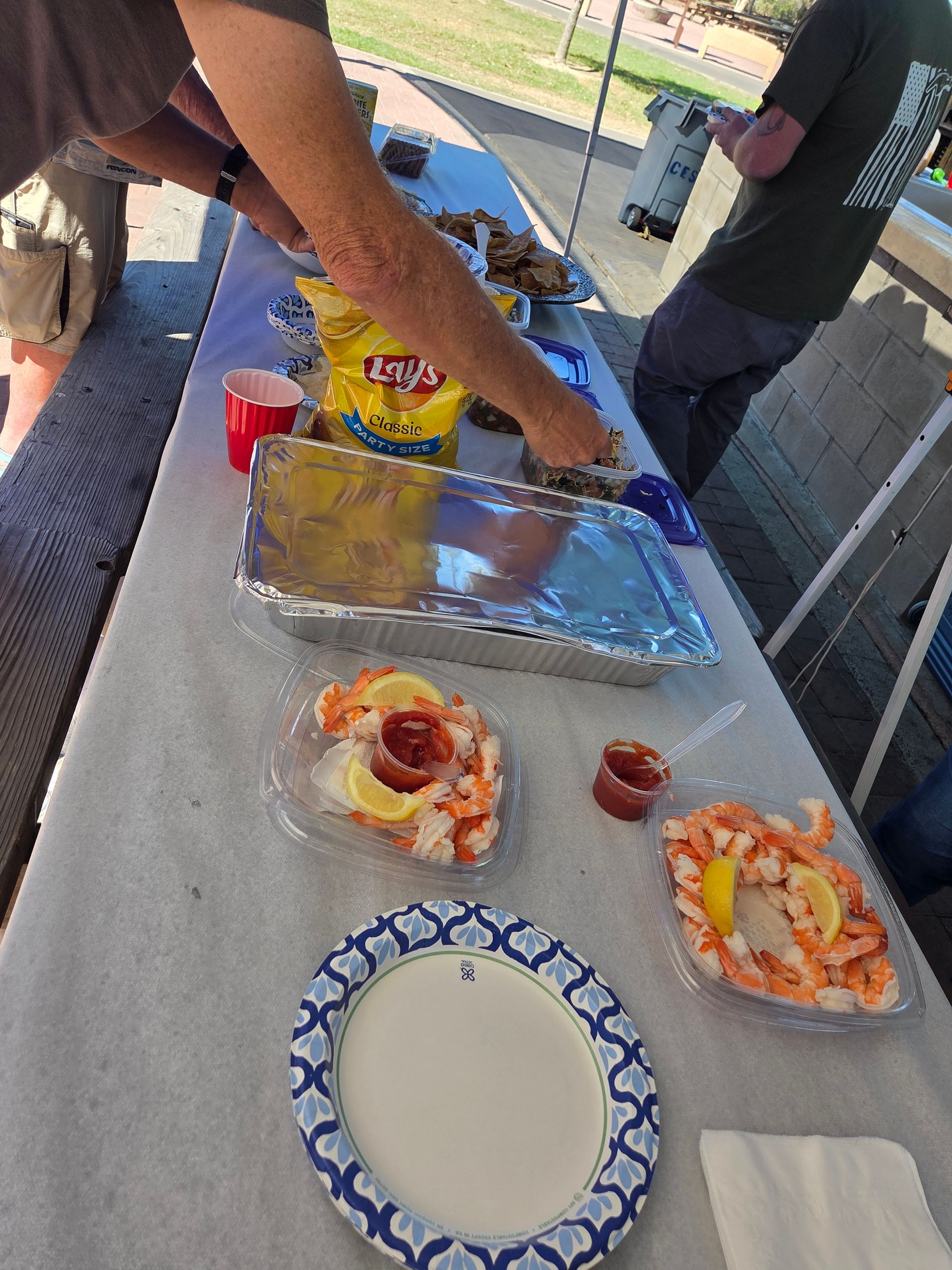 A table laden with food, including shrimp, chips, and a person's hands reaching.