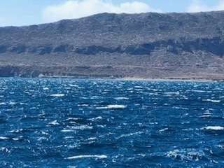 Rough blue sea with whitecaps, dark mountain range in the background.