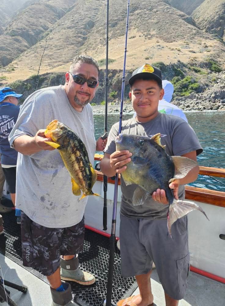People fishing at night from a boat. Black water, fishing rods, and a tackle box are visible.