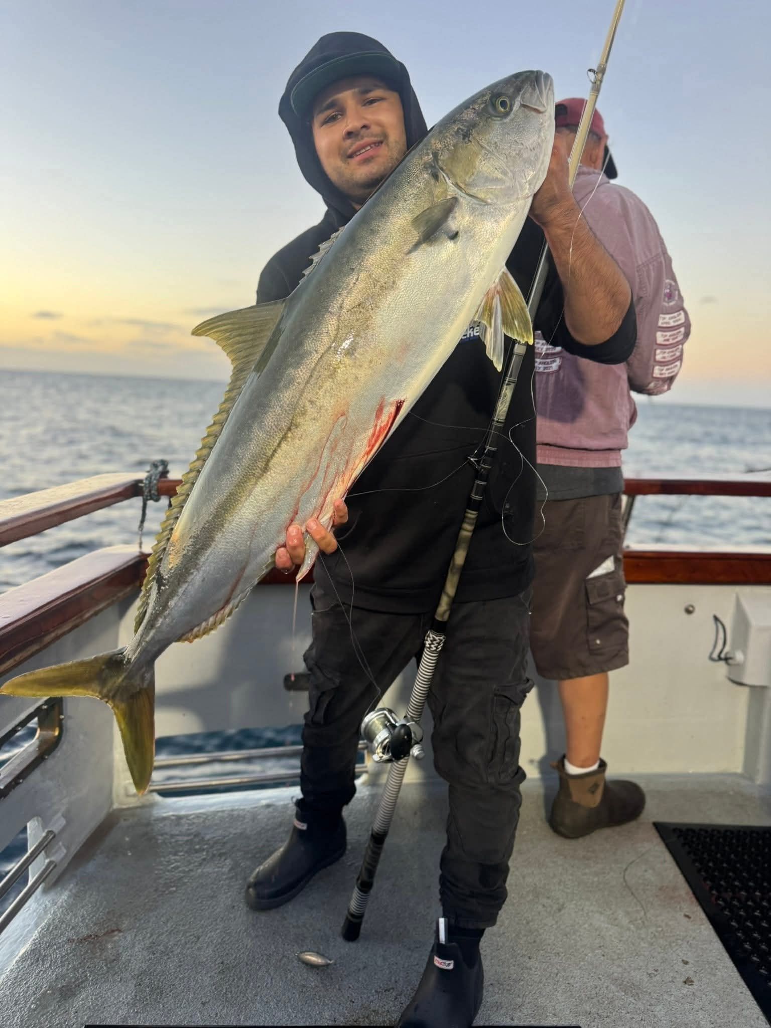 Man on boat holds up large fish. Ocean background. Sunset colors. Fisherman smiles.