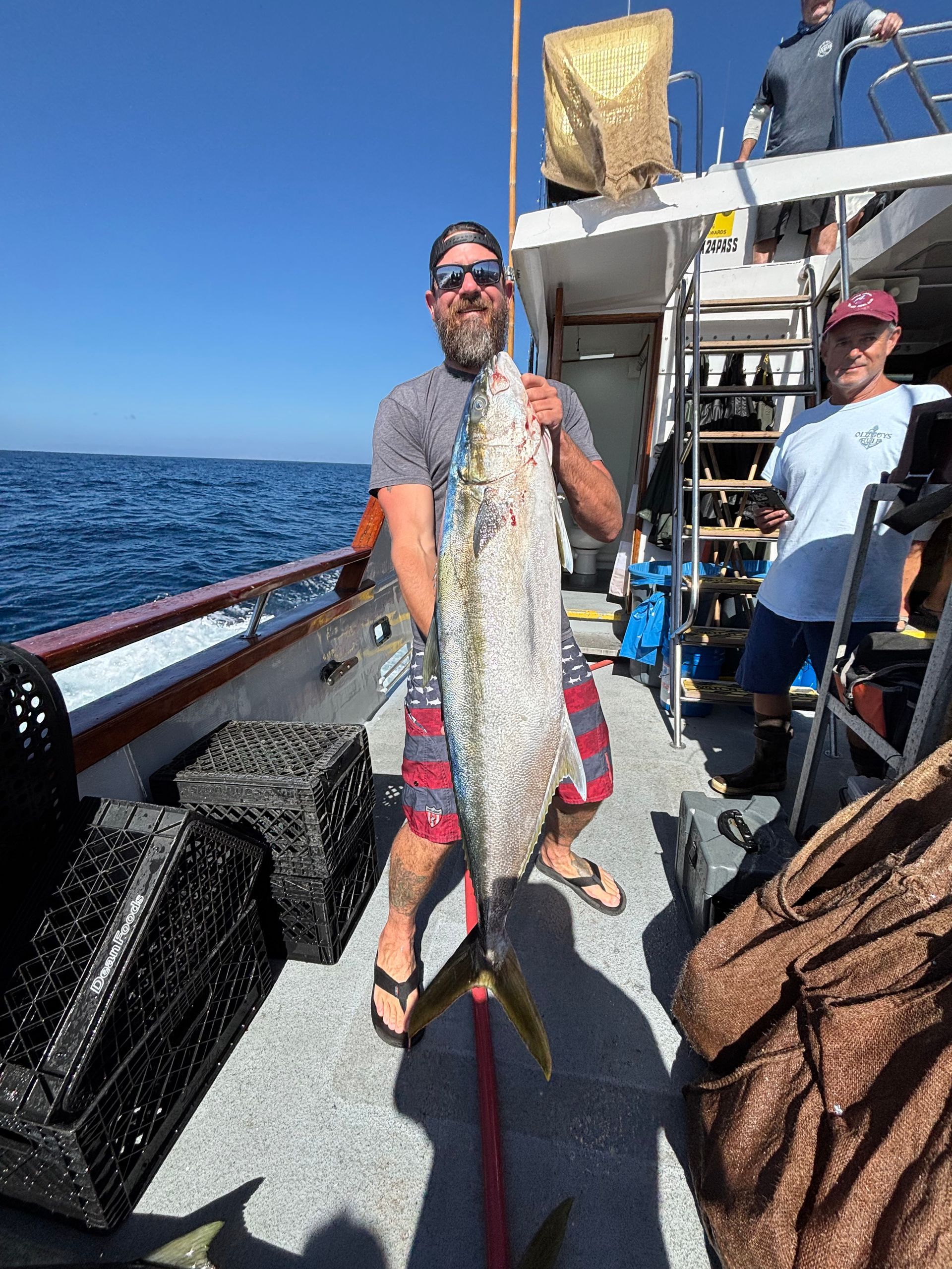 Man on a boat holds up a large fish. Blue water in background.