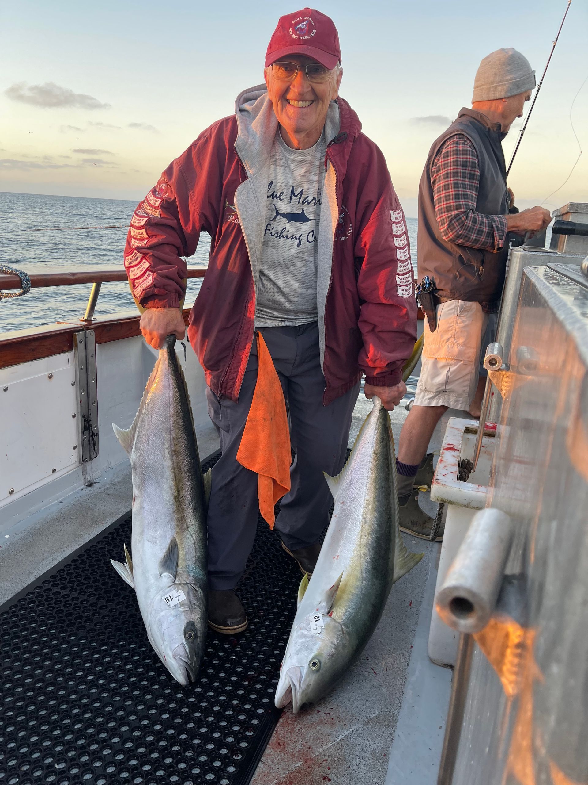 Man holding a large, dark-colored halibut on a boat, sunny day.