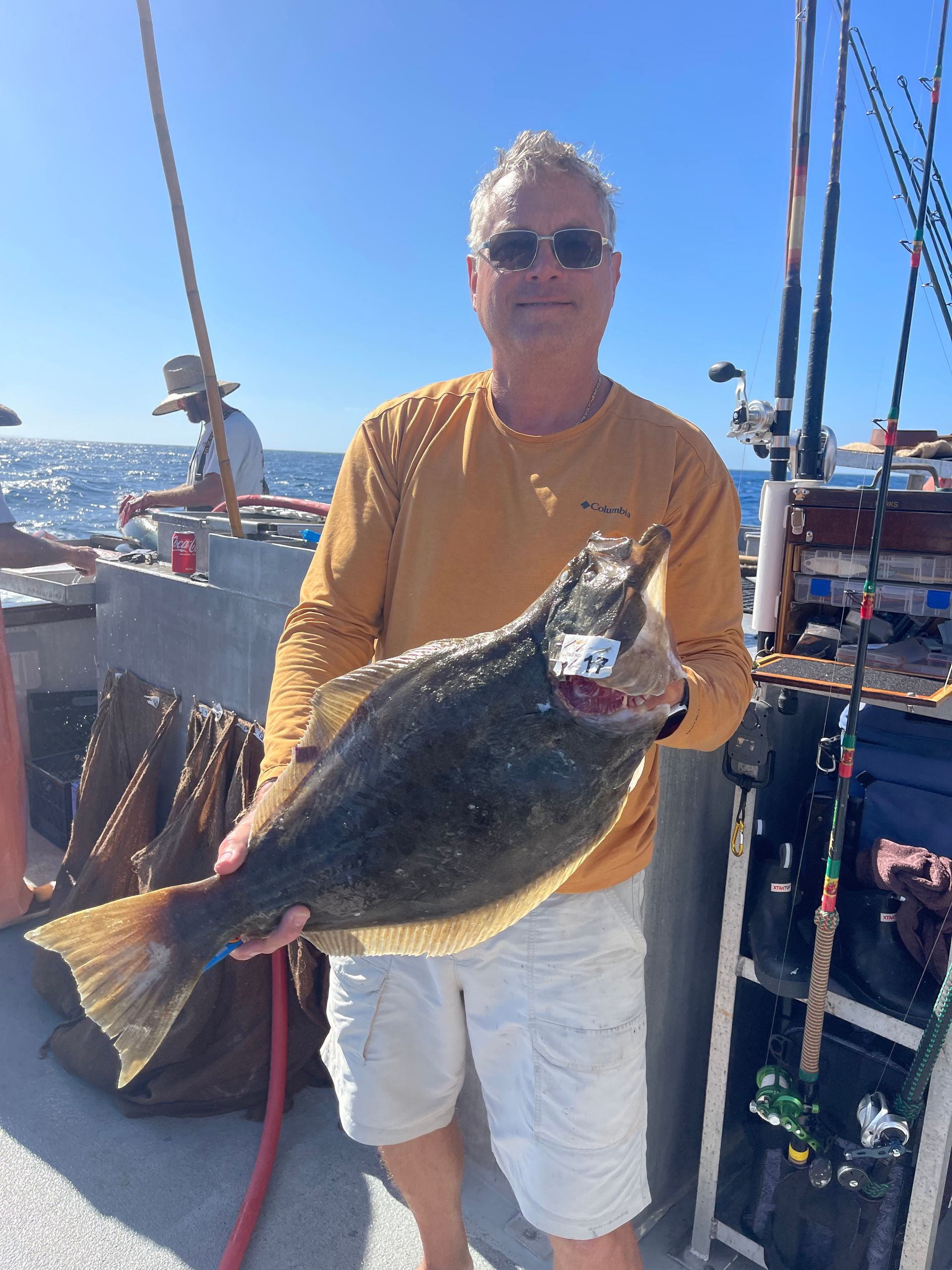 Man holding a large flatfish, smiling on a boat deck.