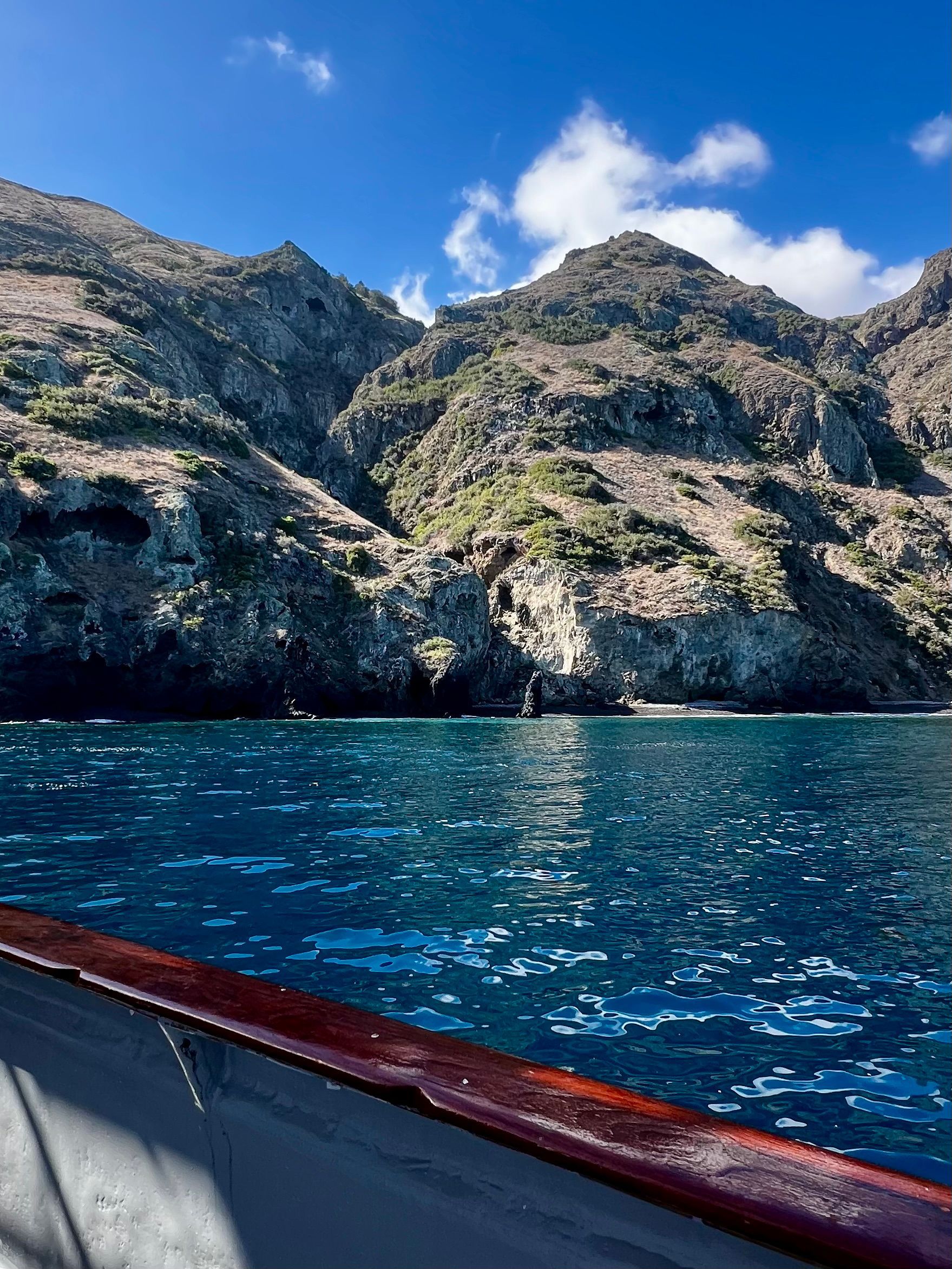 Blue ocean with rocky cliffs under a sunny sky, seen from a boat.