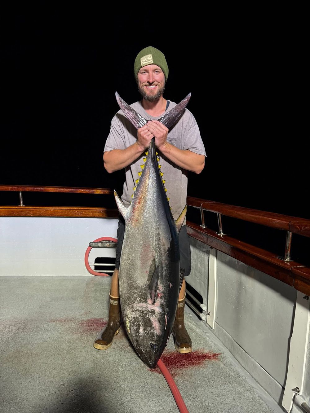 Man holding a large tuna fish on a boat deck at night.