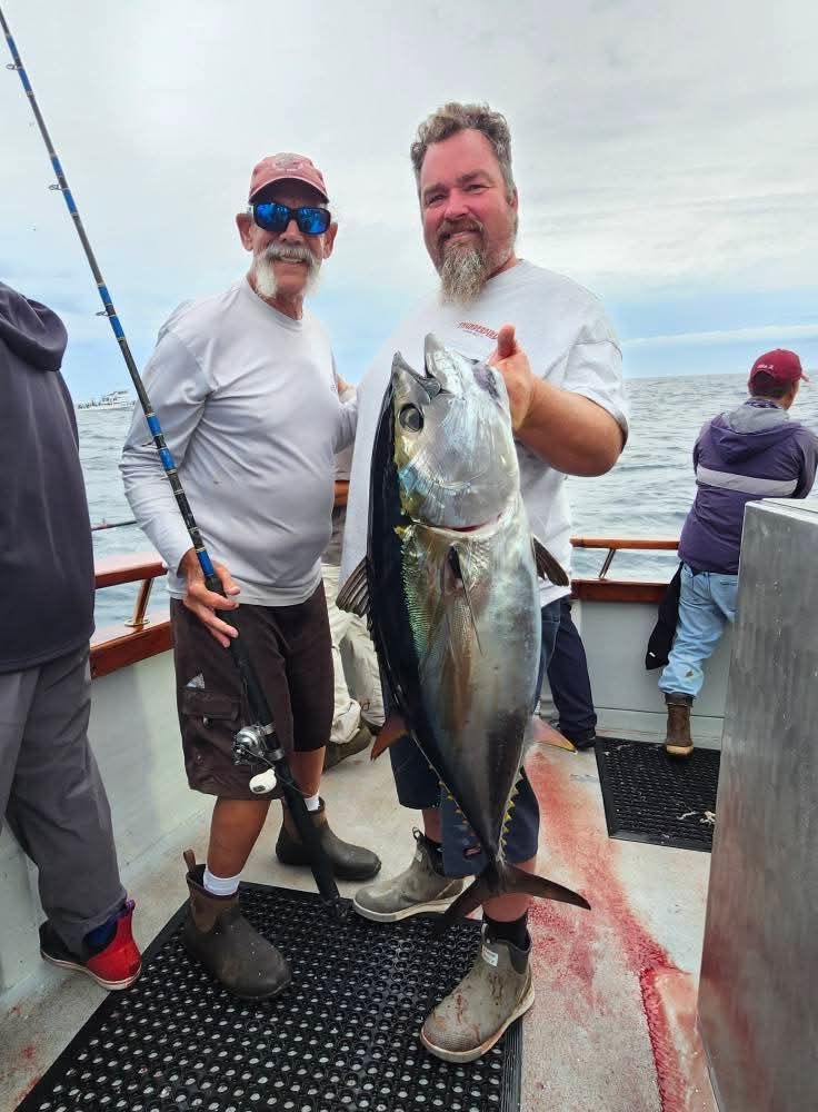 Two men on a boat holding a large speckled fish at night.