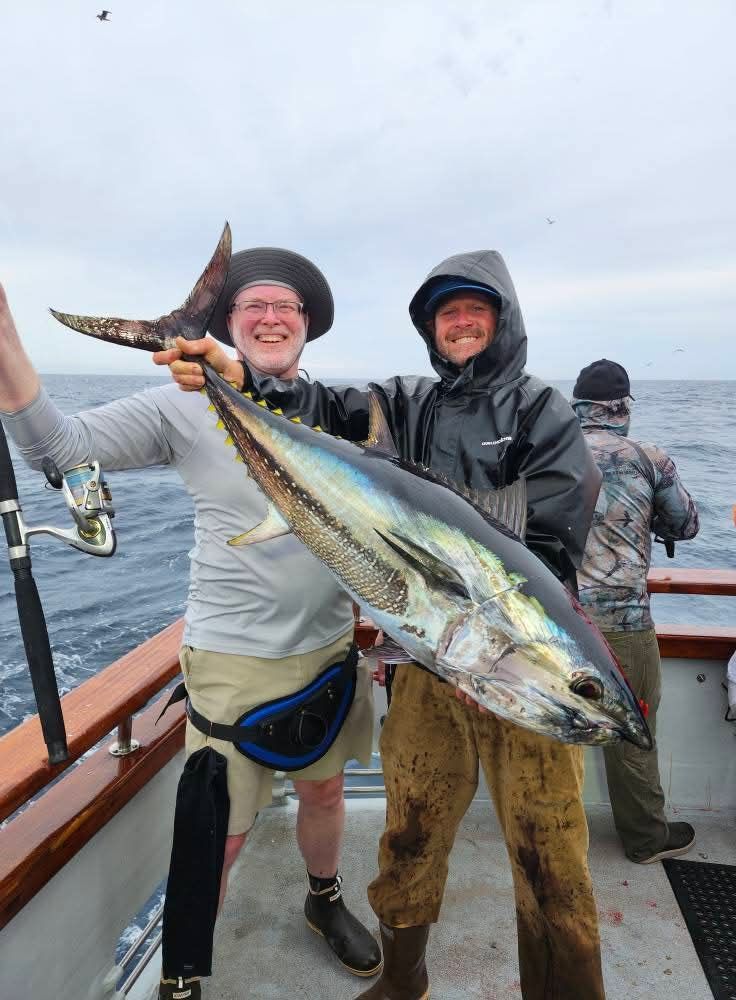 Man on a boat at night holds up a large yellowtail fish. Other people are visible on the boat.