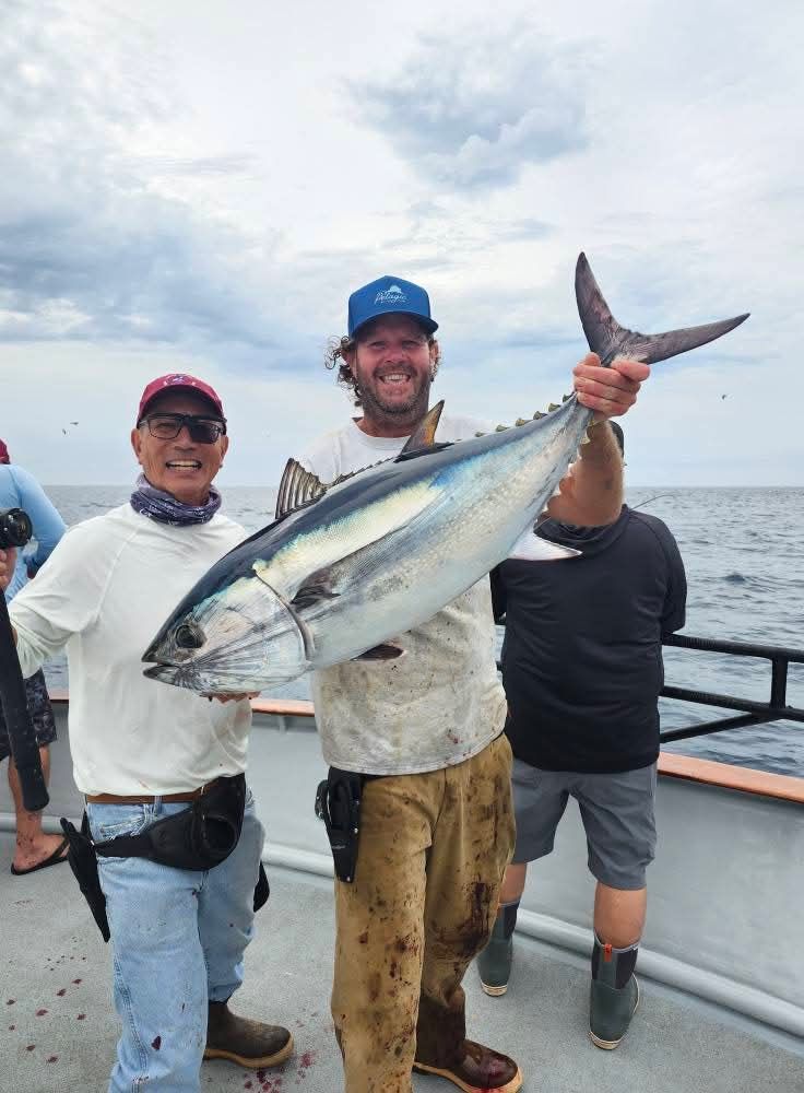 Two men on a boat hold up a freshly caught tuna. Sunny day, blue water.