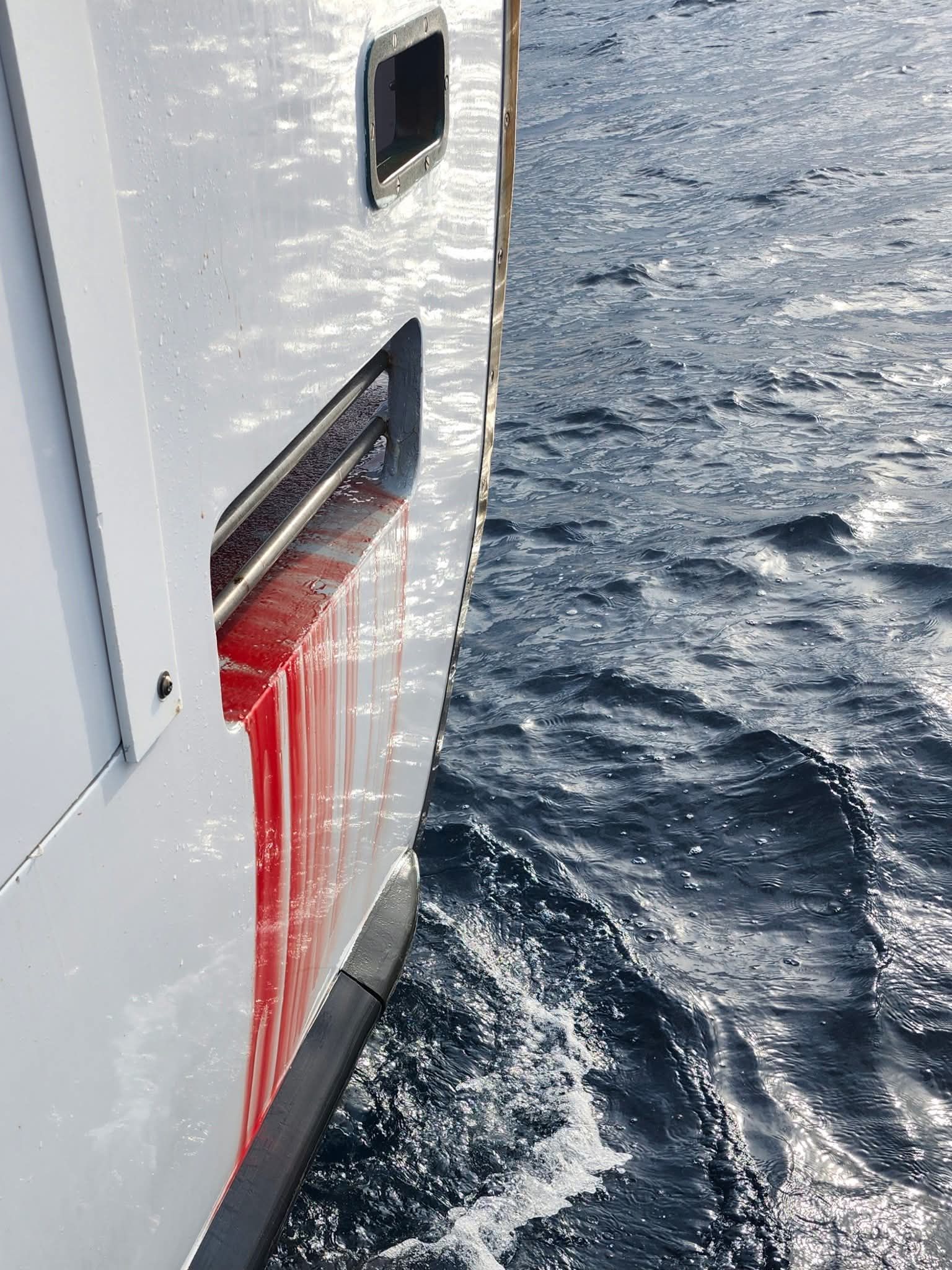 Large tuna fish covered in blood on a boat deck, surrounded by people's feet.