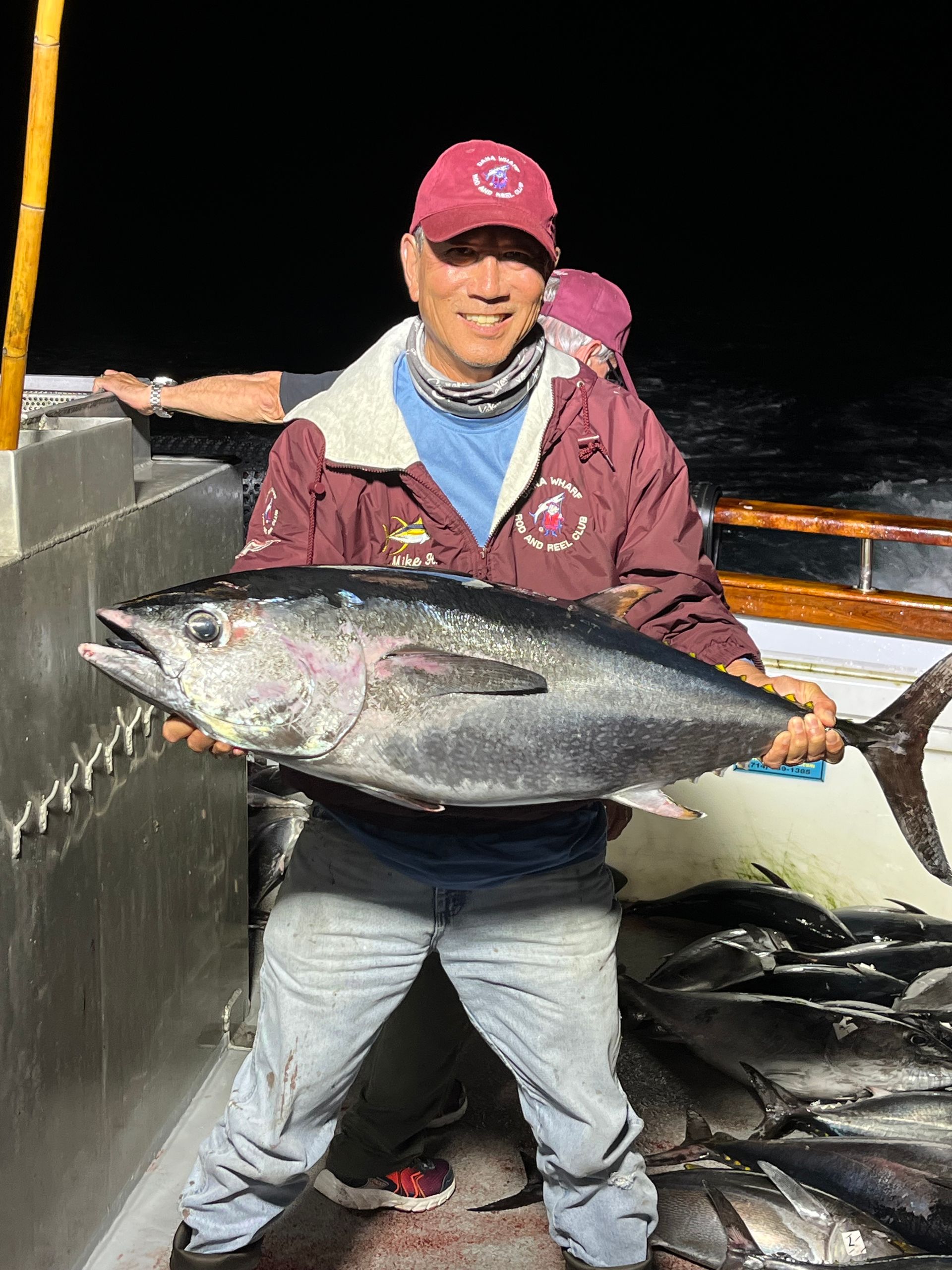 Man on boat at night holding a large tuna fish, smiling.
