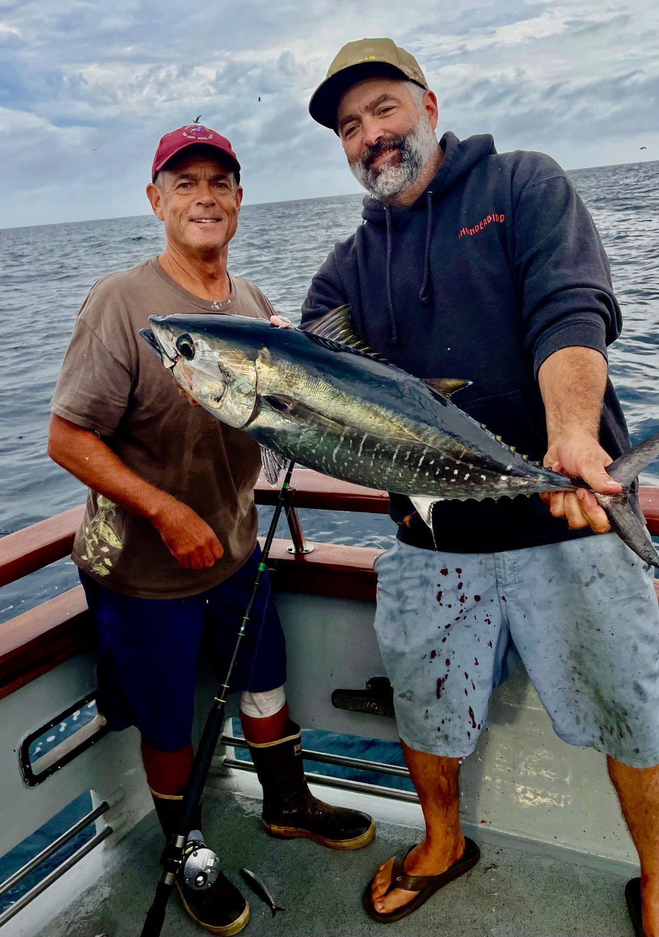 A large fish, covered in blood, lies on a boat deck with wooden trim at night.