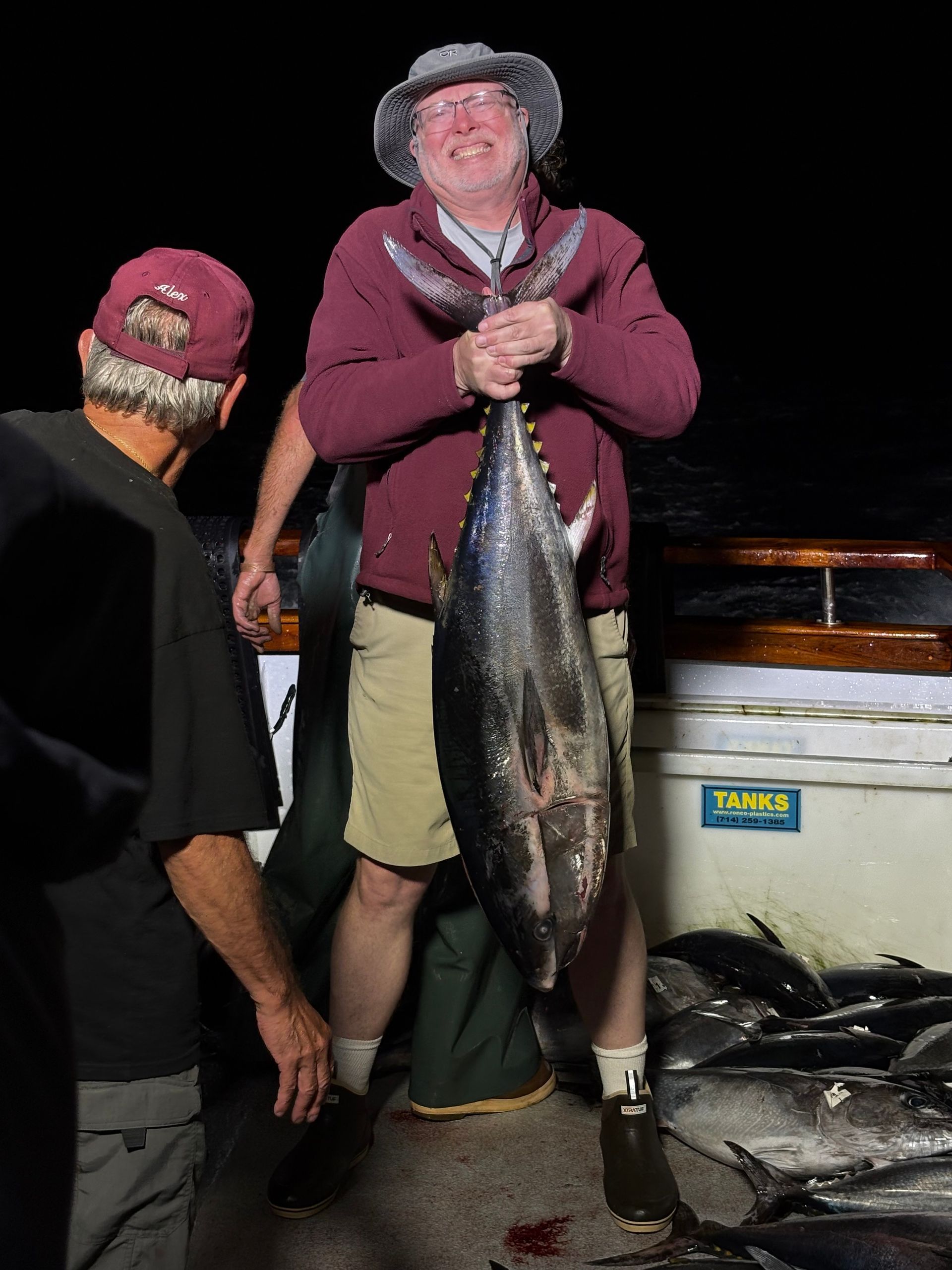 Fished deck filled with a variety of tuna, some hanging, likely at night on a boat.