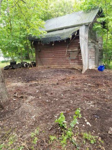 A wooden shed is sitting in the middle of a dirt field in the woods.